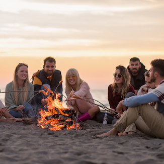 Group Of Young Friends Sitting By The Fire at beach