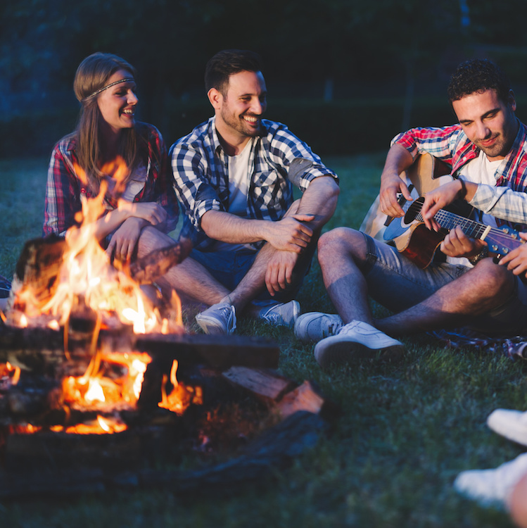 Happy friends playing music and enjoying bonfire