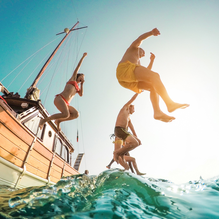 Happy friends diving from sailing boat into the sea - Young people jumping inside ocean in summer excursion day - Vacation, youth and fun concept - Main focus on left man - Fisheye lens distortion