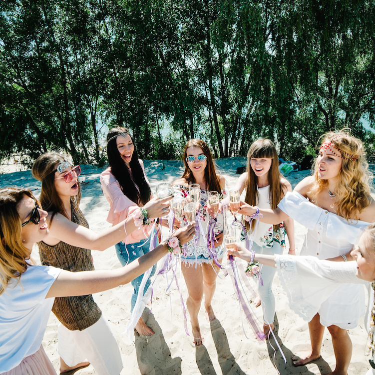 Beautiful happy stylish young girls on sand beach climb glass champagne. Glasses decorated with ribbons flowers. Party in Style boho. Maiden evening Hen-parties. Bachelorette. Close up. Place for text